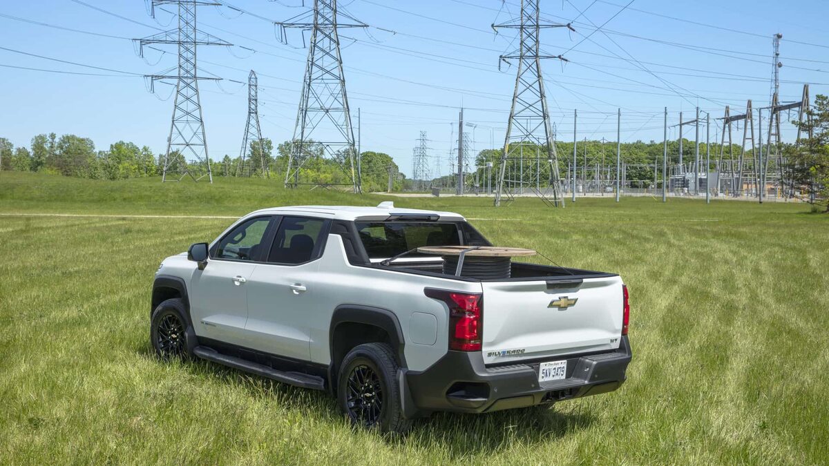 A white 2024 Chevrolet Silverado EV WT4 electric truck parked in a field dotted with transmissio towers