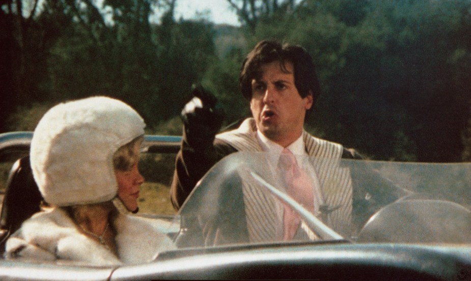 Sylvester Stallone points over the windshield of his car while his passenger watches during the 1975 film "death race 2000" 