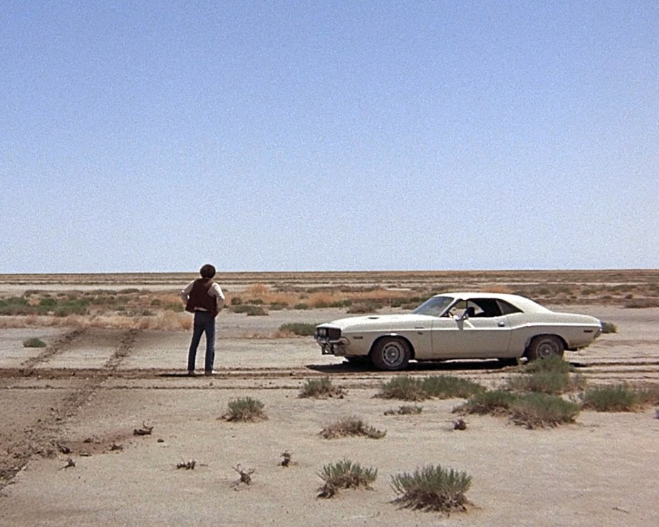 The fugitive Kowalski, played by American actor Barry Newman, stands in the desert next to his white Dodge Challenger in a scene from 'Vanishing Point'