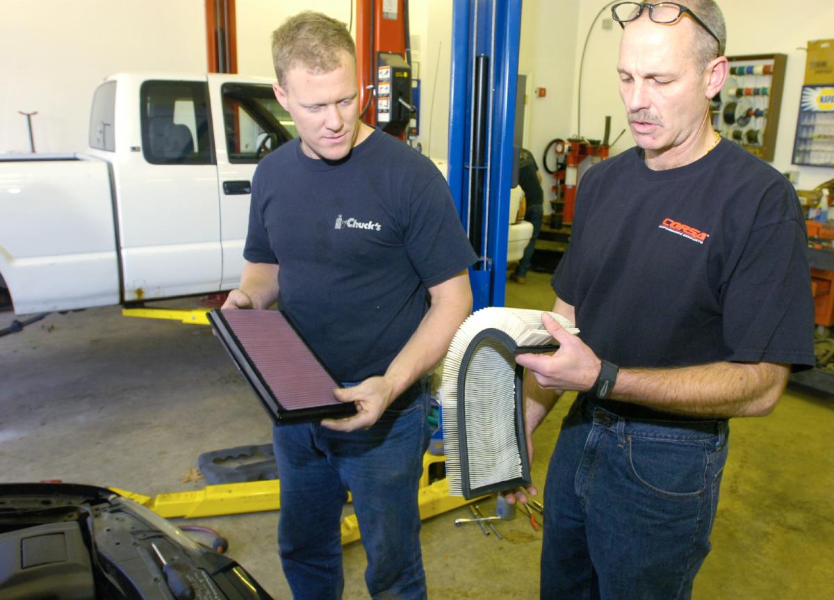 Two mechanics ready to change the air filter on a car.