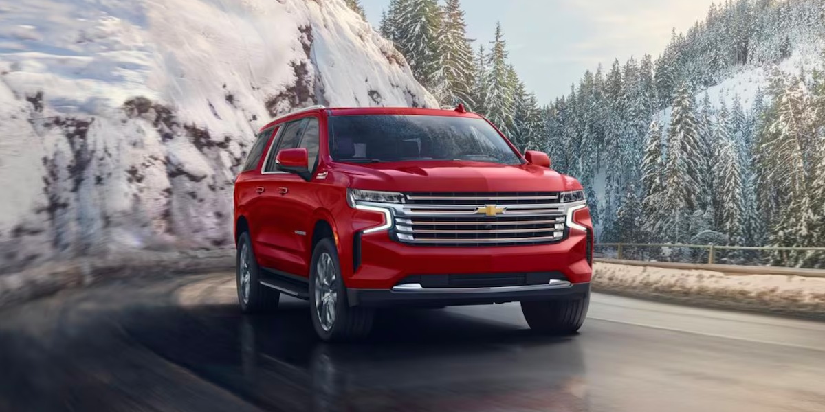 A red 2023 Chevrolet Suburban full-size SUV is driving on the road. 