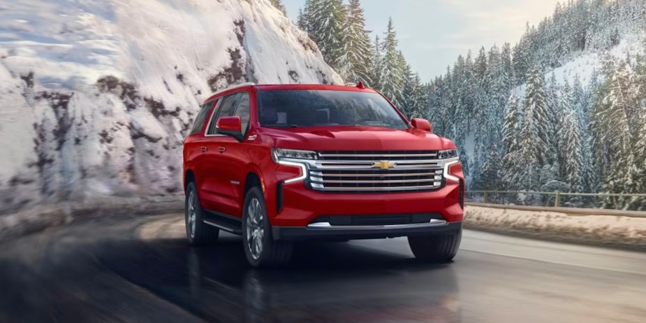 A red 2023 Chevrolet Suburban full-size SUV is driving on the road. 