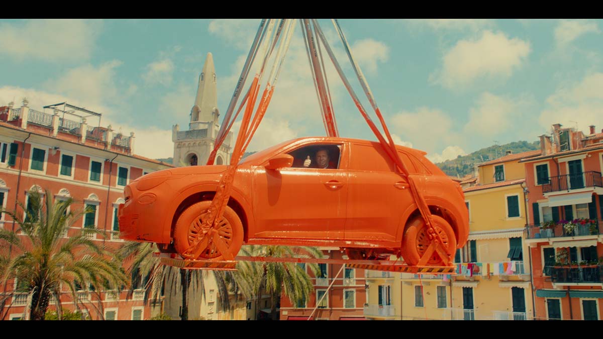 A fiat hanging from a crane after being dipped in paint with CEO inside.