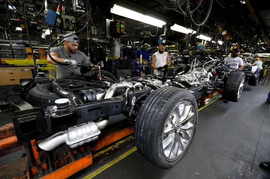 Factory workers assemble the powertrain chassis of a full-frame Ford Explorer SUV, similarly to an F-150 pickup truck