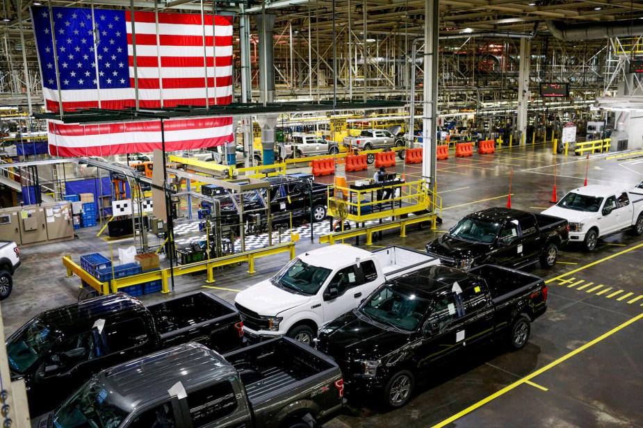 A row of American-made pickup trucks parked under a U.S.A. flag at the Dearborn plant.