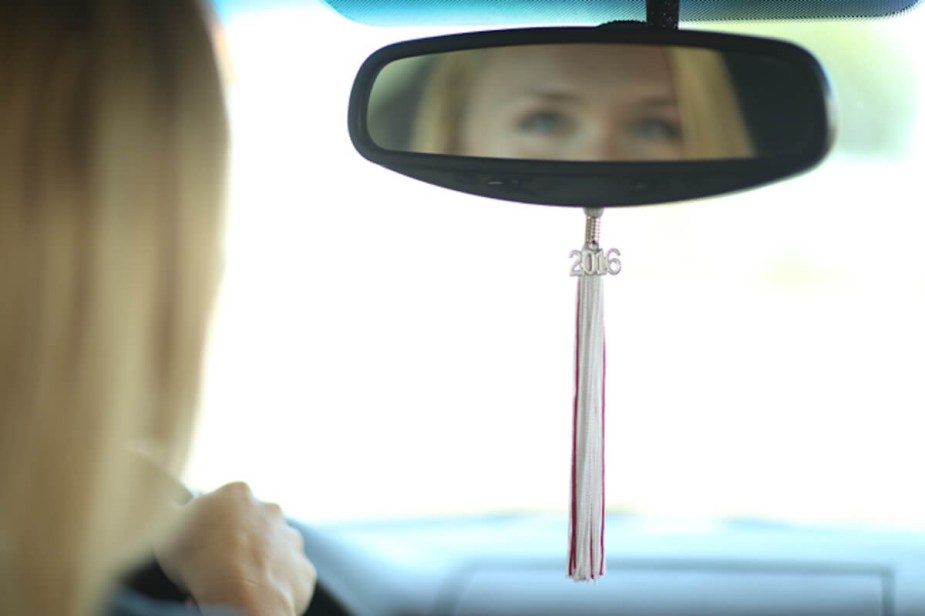 A woman drives a car with a graduation tassel hanging from its rearview mirror.