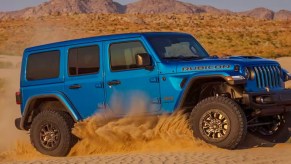 A blue 2023 Jeep Wrangler Rubican 392 is driving in sand.