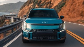 A blue 2024 Kia EV9 fully-electric SUV is driving on the road.