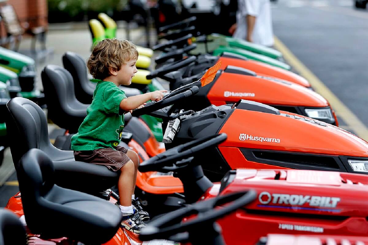 A kid plays on several riding lawn mowers with hydrostatic and automatic transmissions.