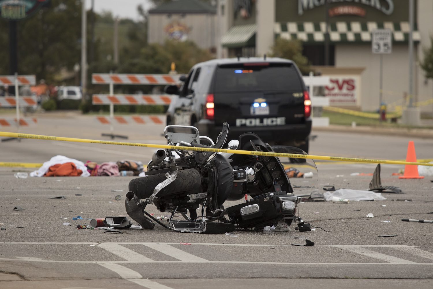 A motorcycle smashed after an accident, a police car and caution tape visible in the background.