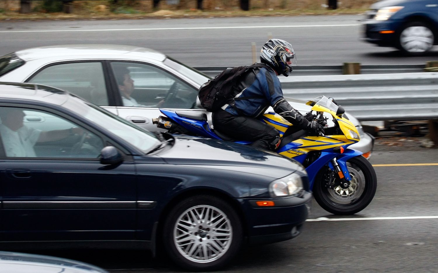 The profile view of a motorcyclist riding between a BMW and another sedan as it splits lanes.