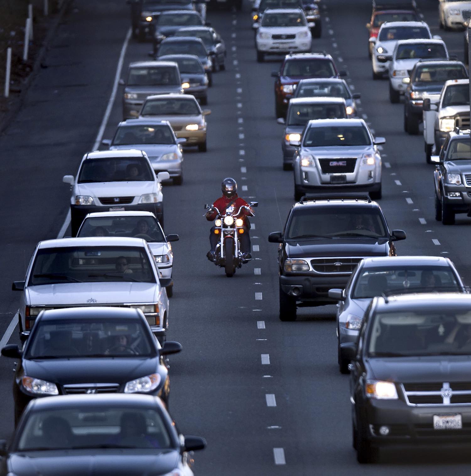 Head-on view of a motorcyclist riding between two lanes of stopped traffic on an interstate highway.