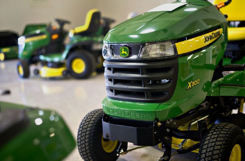 A used green and yellow John Deere X300 riding lawn mower sits on a showroom floor.