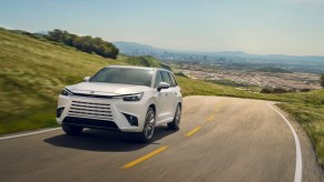 A white 2024 Lexus TX luxury midsize three-row SUV is driving on the road.