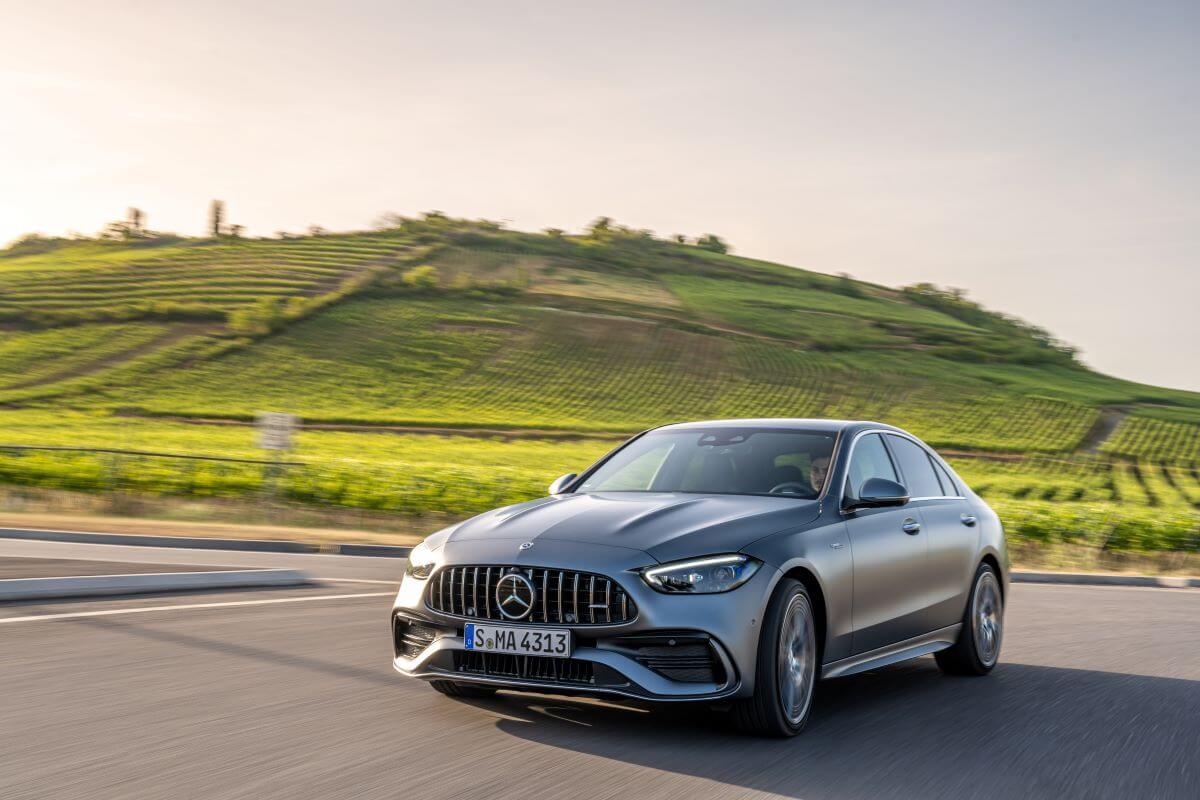 The Mercedes-Benz/Mercedes-AMG C 43 luxury compact sedan model driving past a grass hill of farm fields