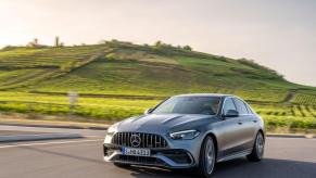 The Mercedes-Benz/Mercedes-AMG C 43 luxury compact sedan model driving past a grass hill of farm fields