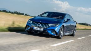 A Mercedes-AMG EQE Sedan European model driving down a country highway past wheat fields