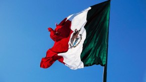 The Mexican national flag flying in front of a blue sky.