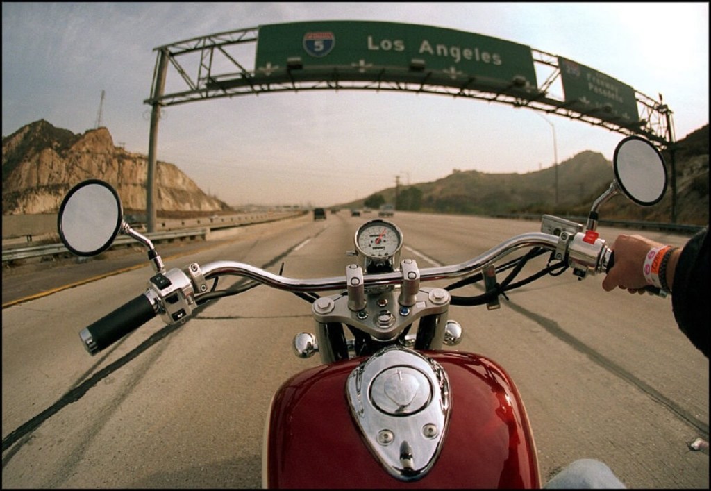 A red motorcycle rides over hot asphalt on an LA freeway. 