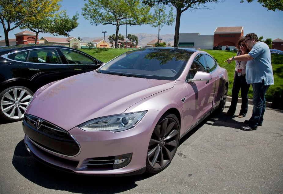 Two Tesla buyers examine a pink Model S on a dealership parking lot.