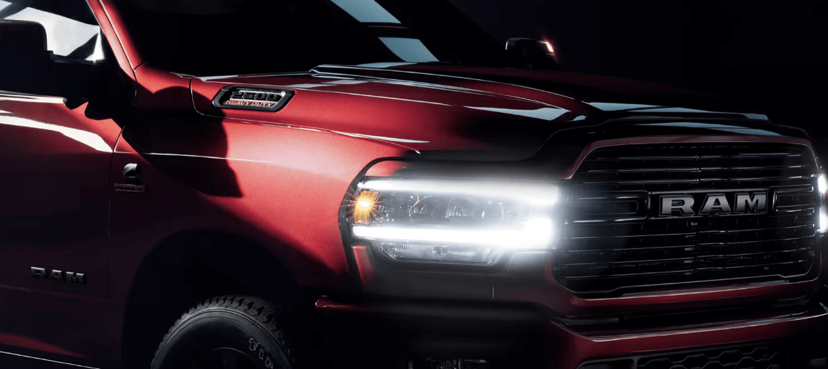 A 2023 Ram 2500 heavy-duty pickup truck model with a red paint color option and its headlights illuminated