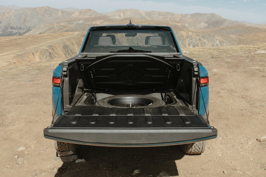 A midsize Rivian electric pickup truck parked on a desert plateau with its tailgate down and its in-bed trunk open.