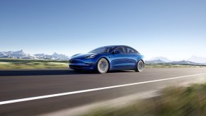 A blue Tesla Model 3 drives down a mountain road with AWD grip.