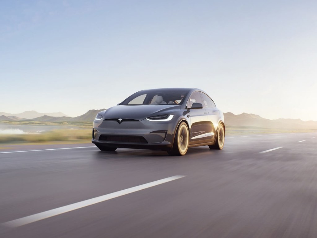 A gray Tesla Model X cruises a sunlit highway.