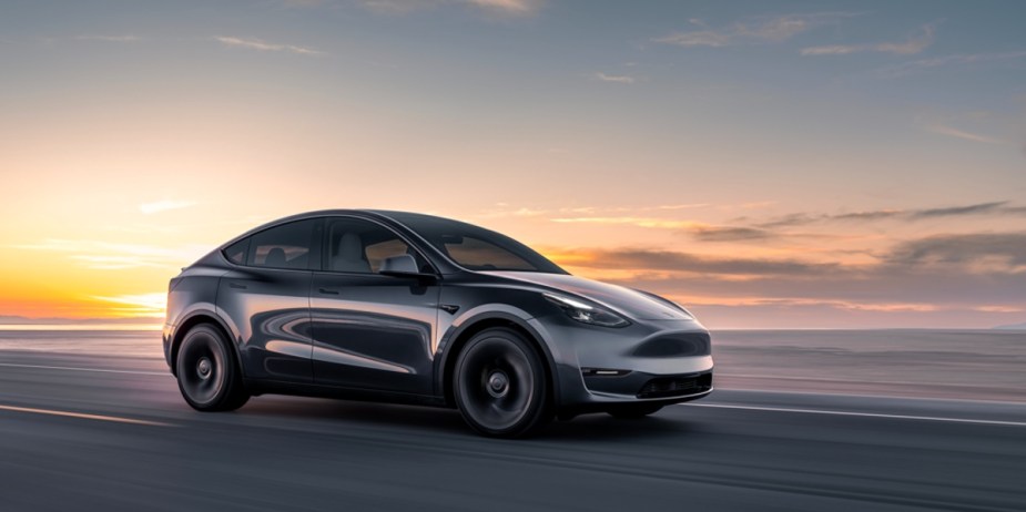 A black 2023 Tesla Model Y small electric SUV is driving on the road. 