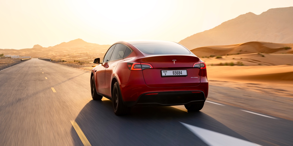 The back of a red Tesla Model Y small electric SUV is driving on the road.