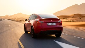 The back of a red Tesla Model Y small electric SUV is driving on the road.
