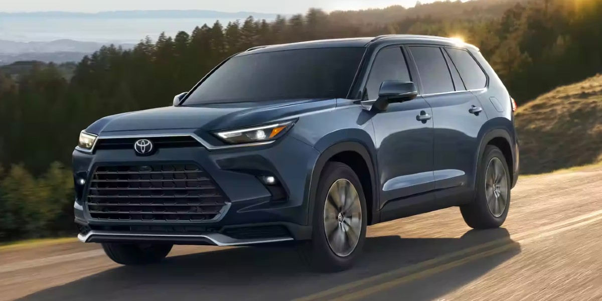 A blue 2024 Toyota Grand Highlander midsize SUV is driving on the road.