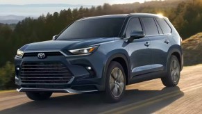 A blue 2024 Toyota Grand Highlander midsize SUV is driving on the road.