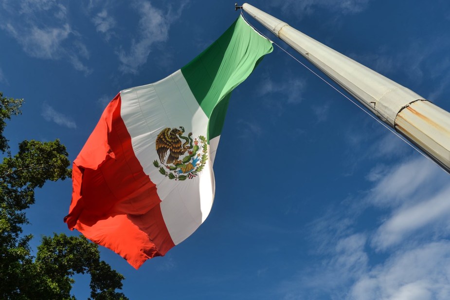 The Mexican flag at the top of a pole, the blue sky visible in the background.