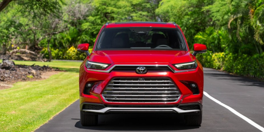 A red 2024 Toyota Highlander three-row midsize SUV is driving on the road.