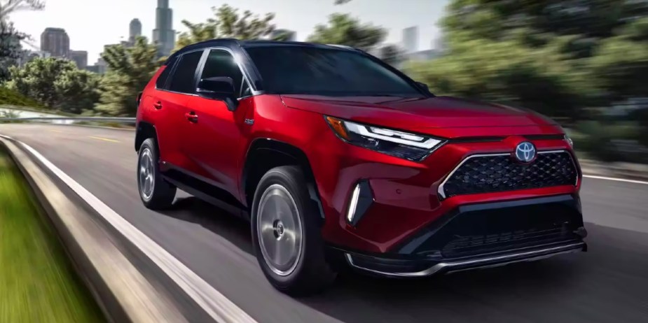 A red Toyota RAV4 Prime small plug-in hybrid SUV is driving on the road. 
