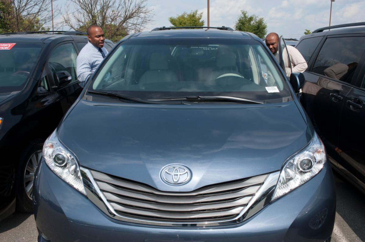 Two men looking at a used Toyota Sienna in a car dealership lot.