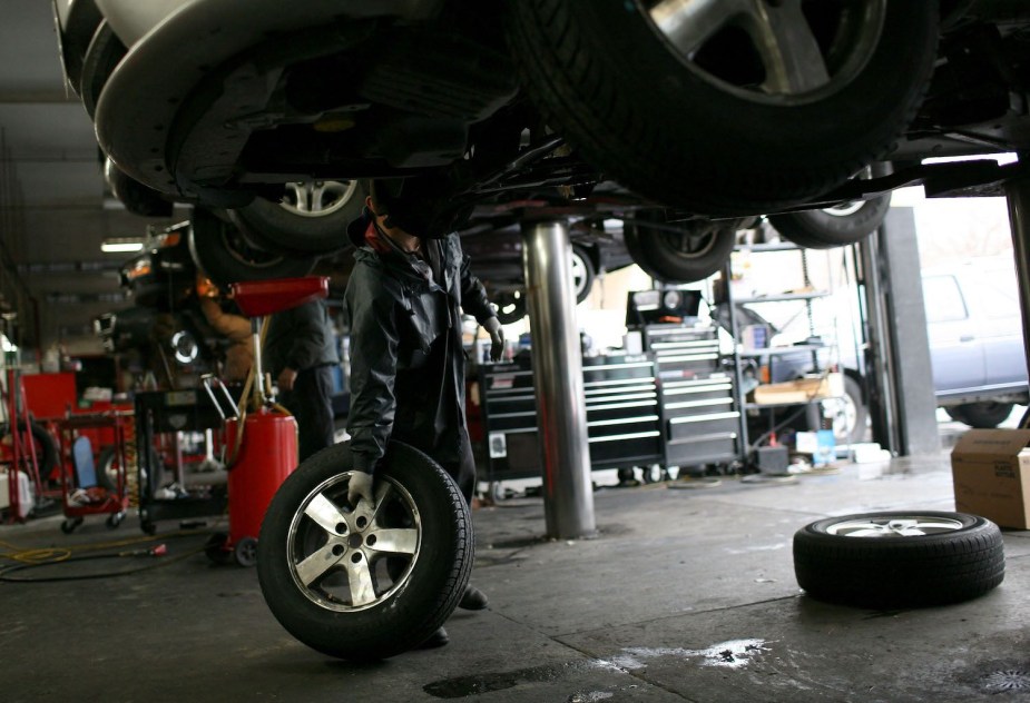 An automotive technician rolls a rim and tire across a mechanic's shop.