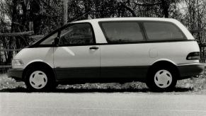 A black and white photo of a Toyota Previa minivan model in side profile parked near a wooden fence