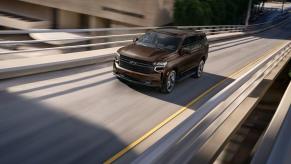A brown 2023 Chevy Tahoe full-size SUV model driving up a highway entry ramp with a blurred background