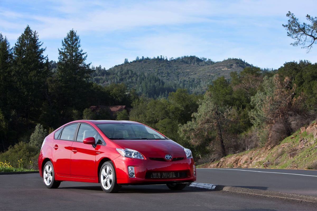 A 2010-2011 model year Toyota Prius hybrid hatchback parked on the side of a forest mountain highway road