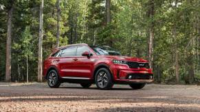 A red 2023 Kia Sorento Hybrid compact SUV model parked on a gravel plateau in a forest