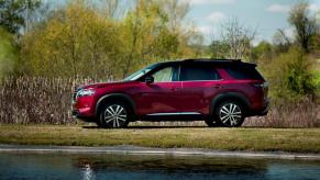 A side profile shot of a 2023 Nissan Pathfinder midsize SUV model parked on a grass shore near a small lake or pond