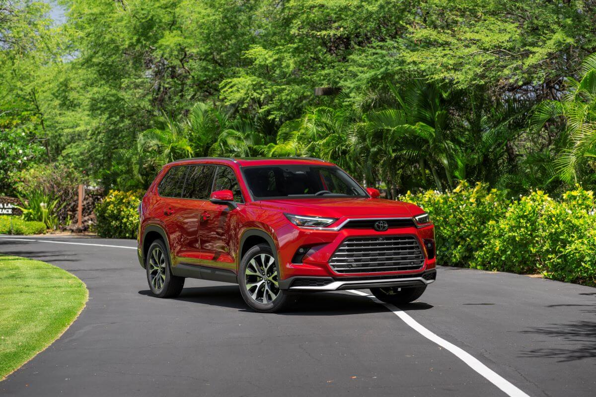 The 2024 Toyota Grand Highlander Platinum in Ruby Flare Pearl paint color option parked near lush green trees