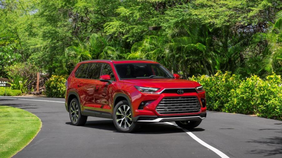 The 2024 Toyota Grand Highlander Platinum in Ruby Flare Pearl paint color option parked near lush green trees