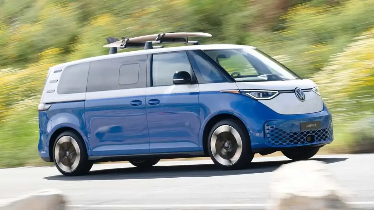 blue id.Buzz U.S. spec EV driving at speed with a surf board up top.