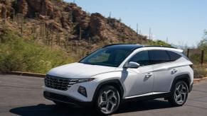 A 2023 Hyundai Tucson Hybrid compact SUV model in white driving in a desert environment with cacti