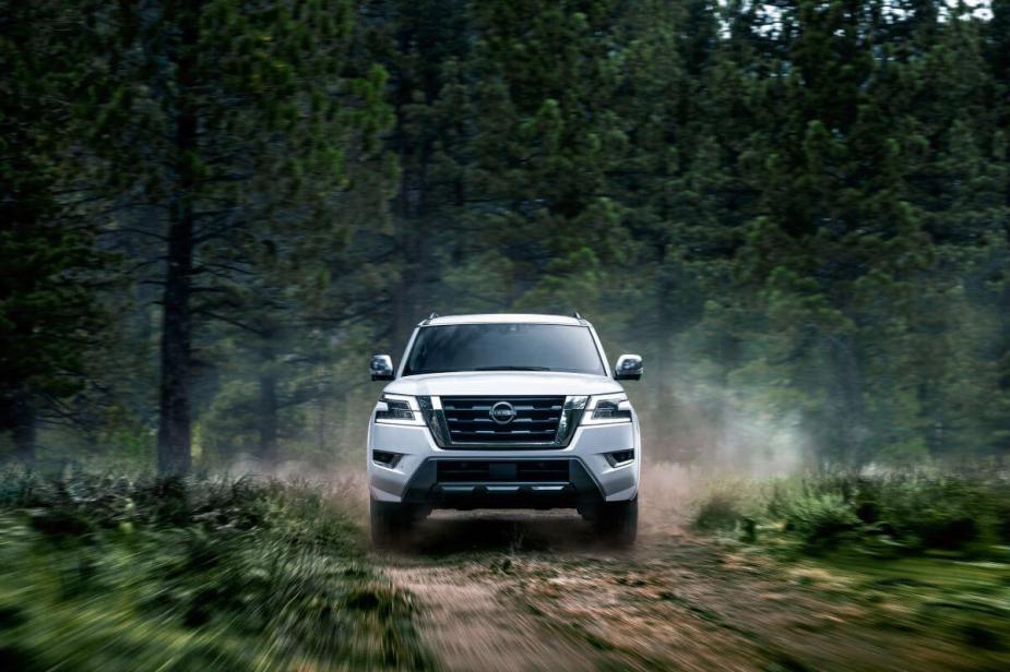 A 2023 Nissan Armada full-size SUV model driving on a trail within a deep green forest of evergreens