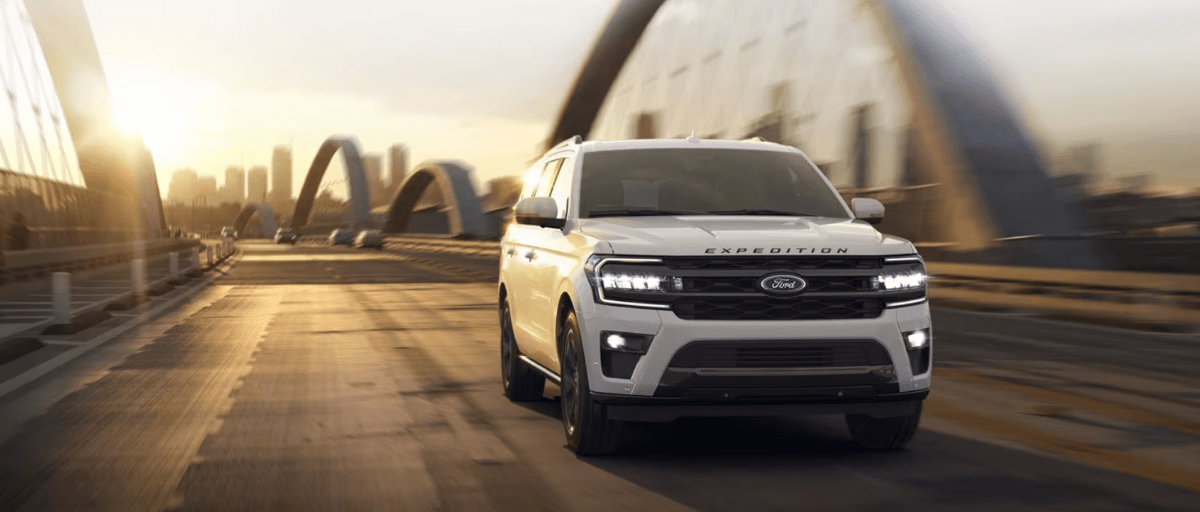 A 2024 Ford Expedition full-size SUV model driving over a bridge as the sun sets