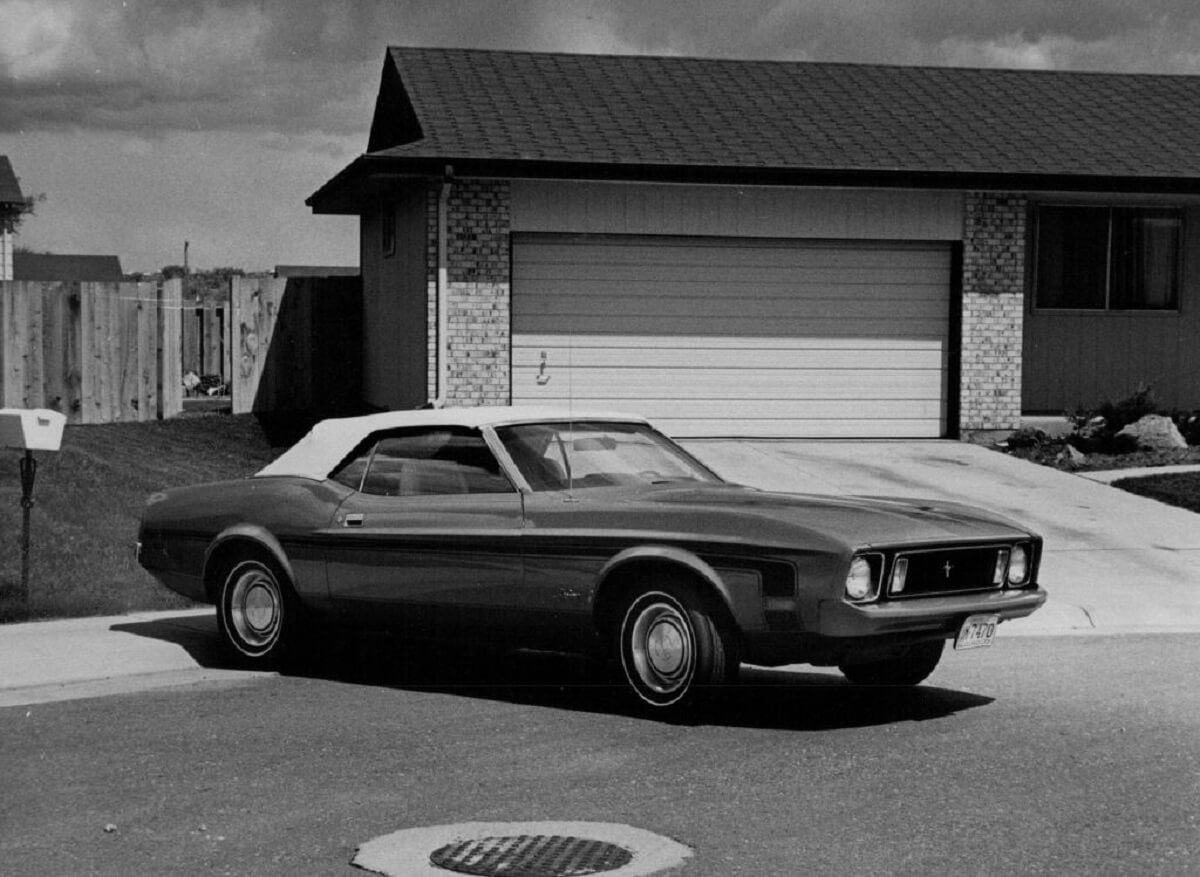 A 1973 Ford Mustang parks next to an attached garage.
